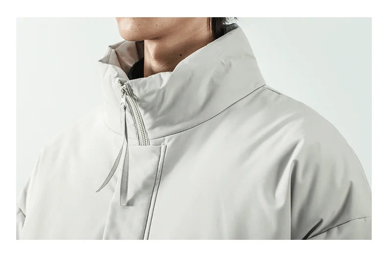 Close-up of a person wearing a light gray high-collar jacket with a zippered neck and drawstring detail, shown against a plain light gray background.