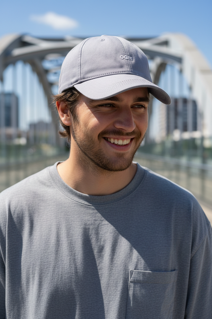 Man wearing a gray cap and shirt standing in front of a bridge