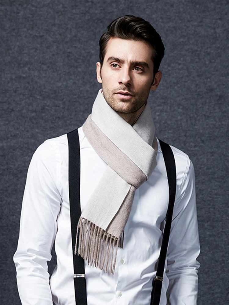 A man wearing a white dress shirt, black suspenders, and a light beige scarf with fringe, posed against a textured gray background.
