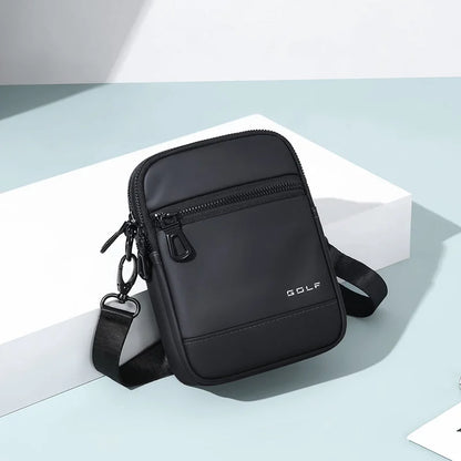 A black nylon crossbody bag with a front zippered pocket and a small white 'GOLF' logo, displayed on a white geometric block against a light blue-gray background.