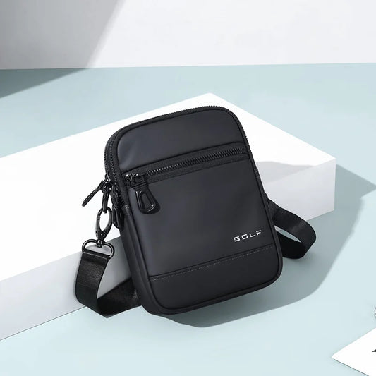 A black nylon crossbody bag with a front zippered pocket and a small white 'GOLF' logo, displayed on a white geometric block against a light blue-gray background.