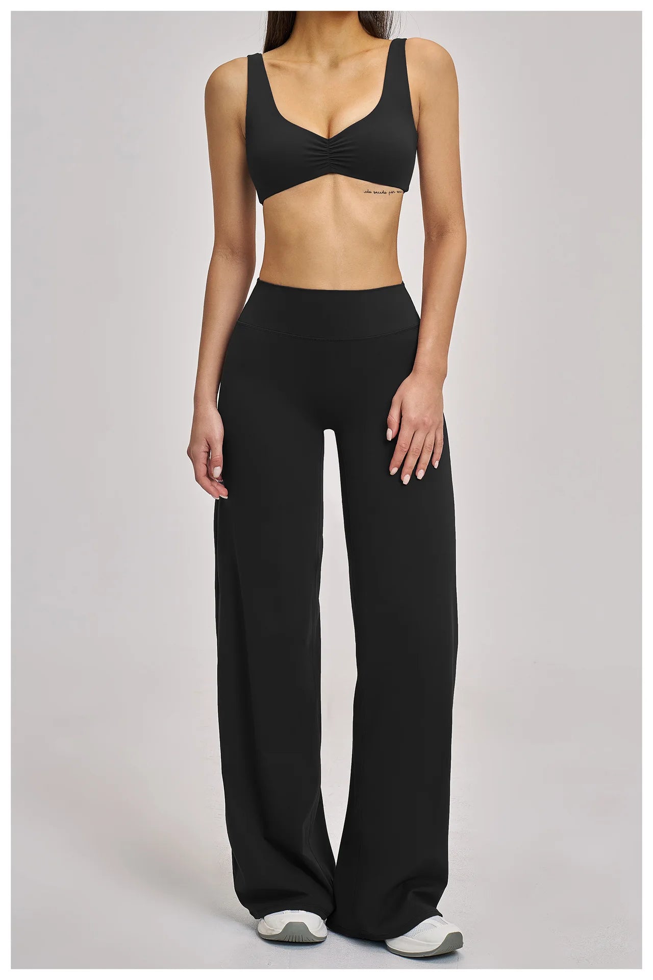 Person wearing a black sports bra and wide-leg pants on a gray background