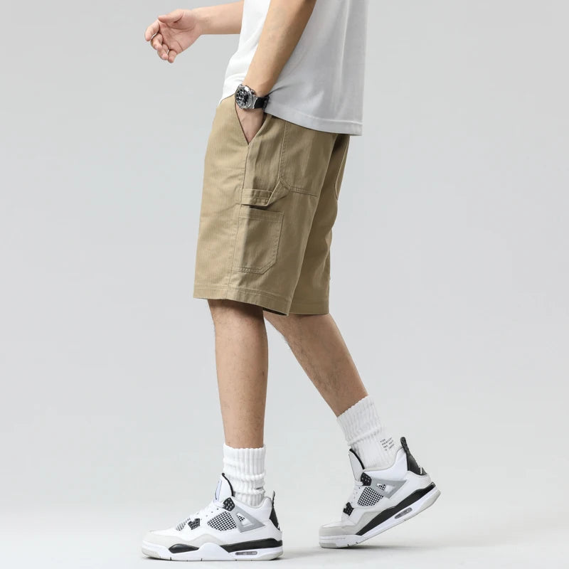 Person wearing beige cargo shorts, white sneakers, and a white shirt on a plain background