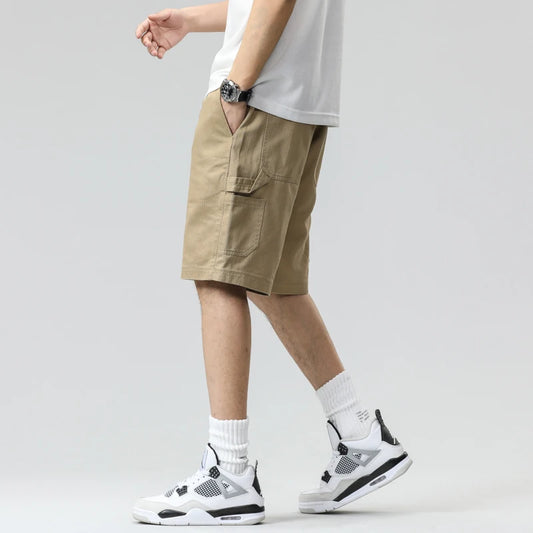 Person wearing beige cargo shorts, white sneakers, and a white shirt on a plain background