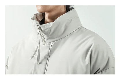 Close-up of a person wearing a light gray high-collar jacket with a zippered neck and drawstring detail, shown against a plain light gray background.