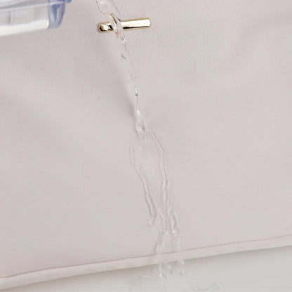 Close-up of a pale blush pink fabric surface with a small gold metal accent and a clear liquid being poured over it to demonstrate water resistance.