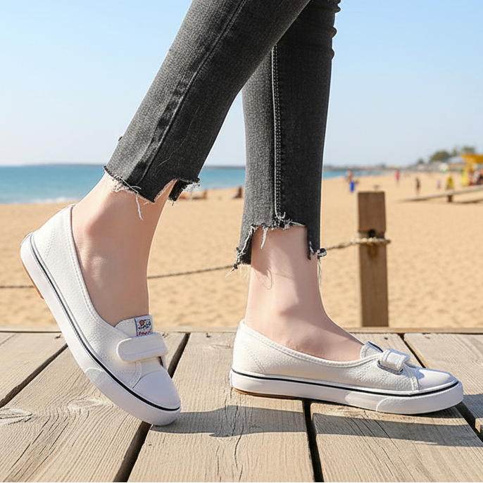 Person wearing white sneakers on a wooden deck with a beach and colorful buildings in the background