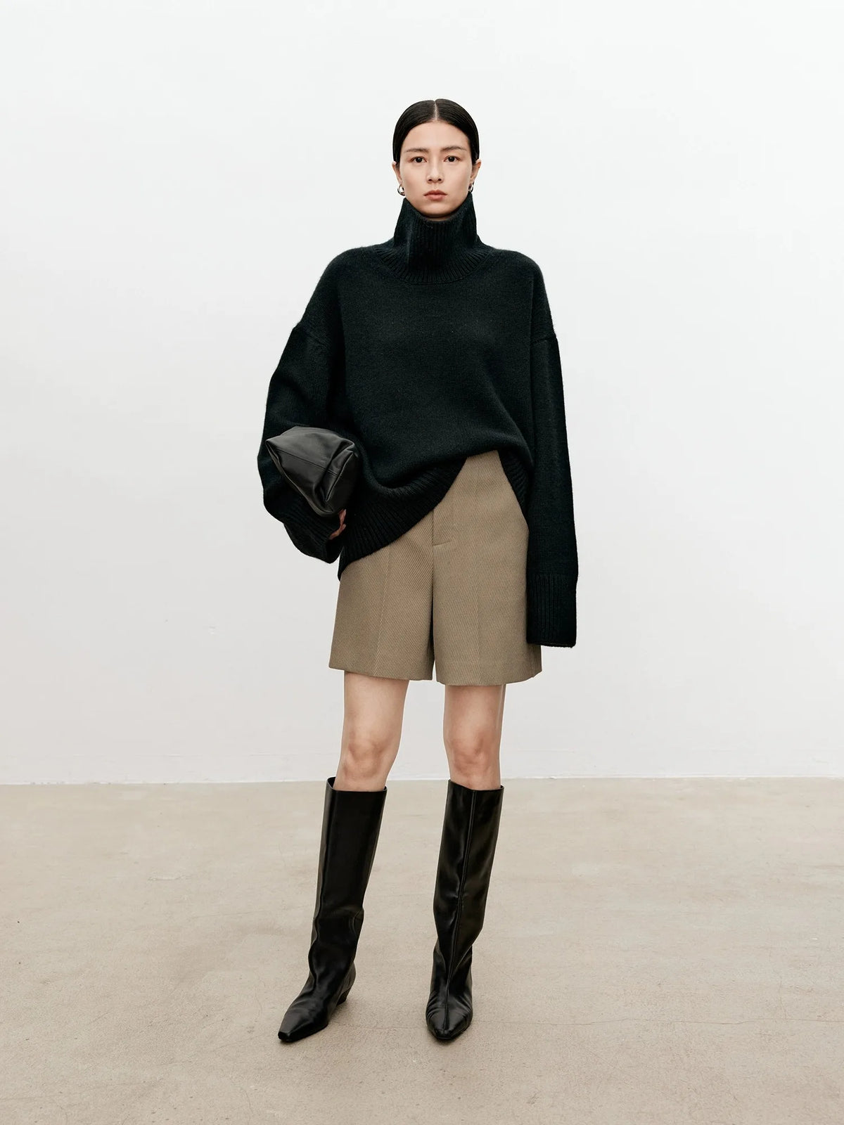 Person wearing a black sweater, beige shorts, and black boots on a plain background