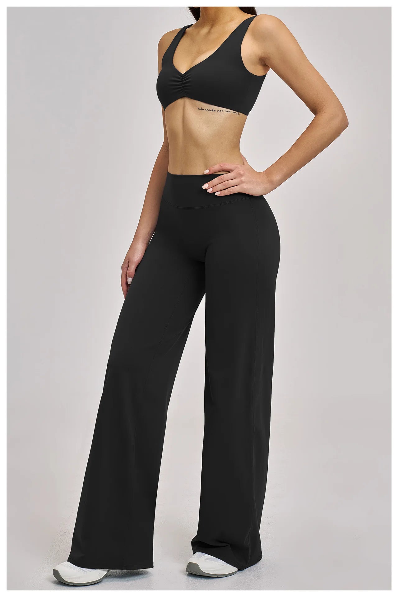 Person wearing a black sports bra and high-waisted black leggings on a light gray background