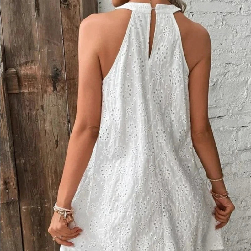 White dress with floral patterns worn by a person, standing against a wooden and brick wall.