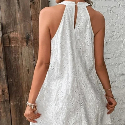 White dress with floral patterns worn by a person, standing against a wooden and brick wall.