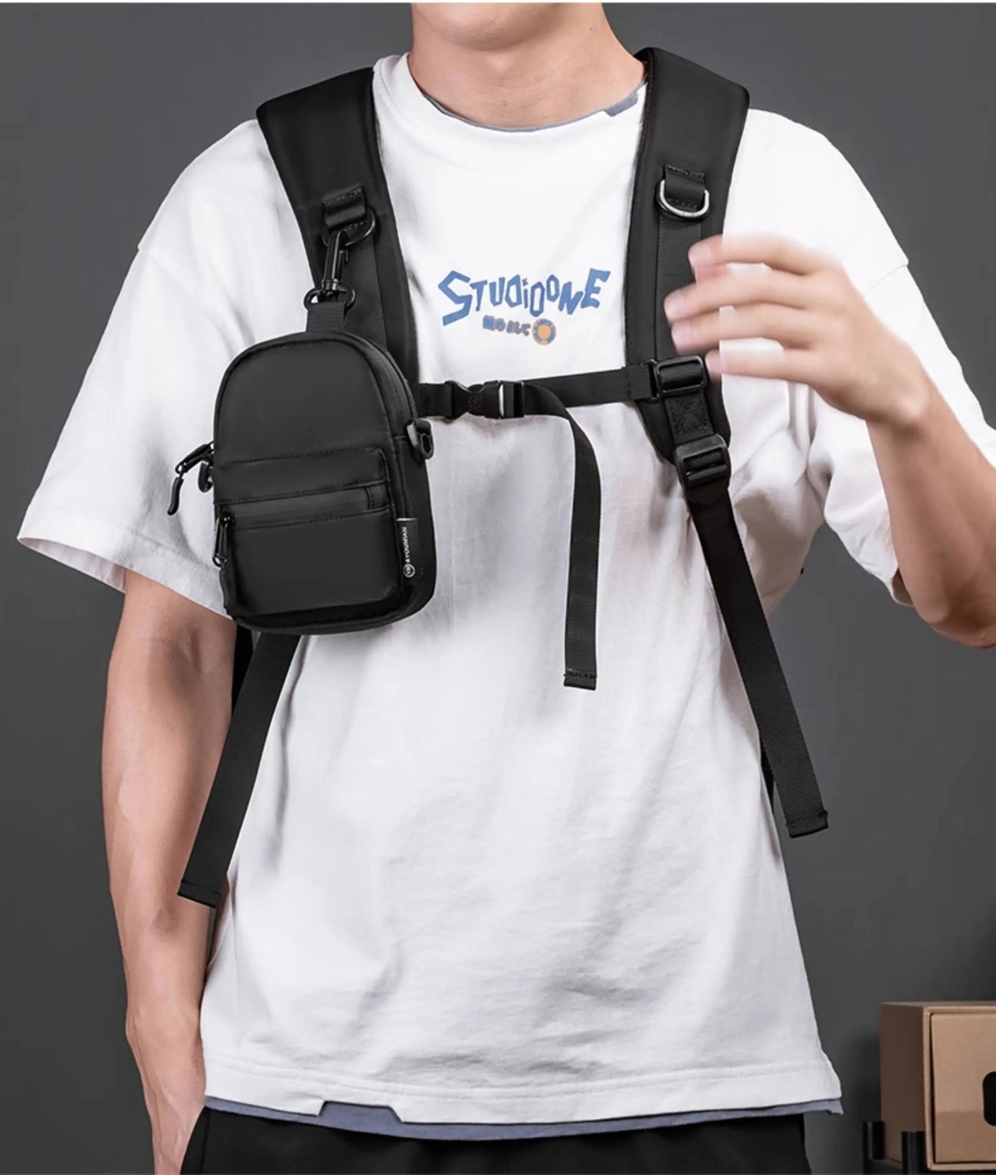 Person wearing a black crossbody bag over a white t-shirt with blue text.