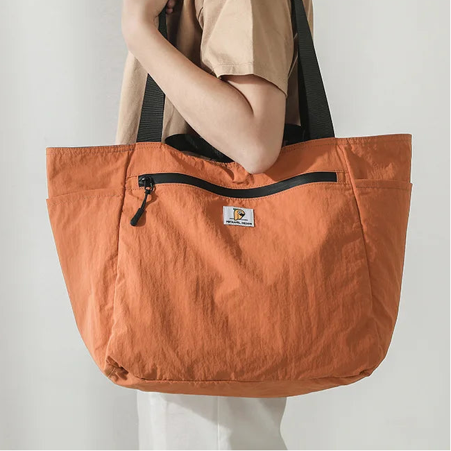 Person holding an orange tote bag with a visible brand logo against a plain background