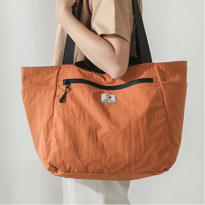 Person holding an orange tote bag with a visible brand logo against a plain background