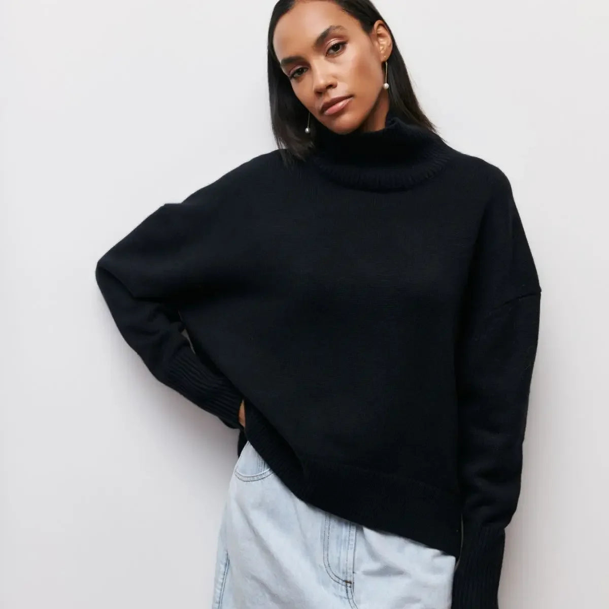Person wearing a black turtleneck sweater and light blue jeans on a plain background
