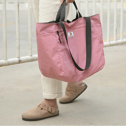 Person holding a pink tote bag with black straps on a light surface.