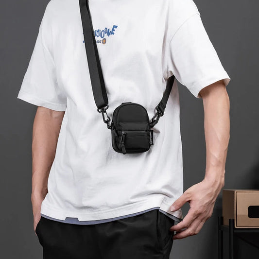 Person wearing a white t-shirt with a black camera bag over their shoulder against a gray background