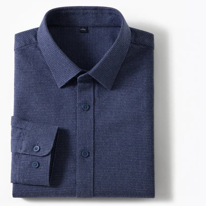 A folded navy blue long-sleeve dress shirt with a subtle textured waffle or micro-check pattern, featuring a classic collar, button-down front, and a single cuff with two buttons, shown on a clean white background.