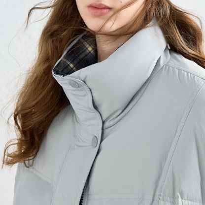 Close-up of a person wearing a light gray puffer jacket with a high collar and snap-button front, showing part of the face, hair, and a plaid lining at the collar.