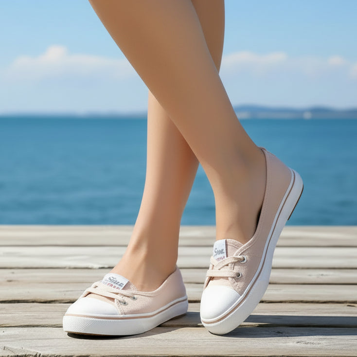 Beige loafers worn by a person on a wood deck with sea in the background