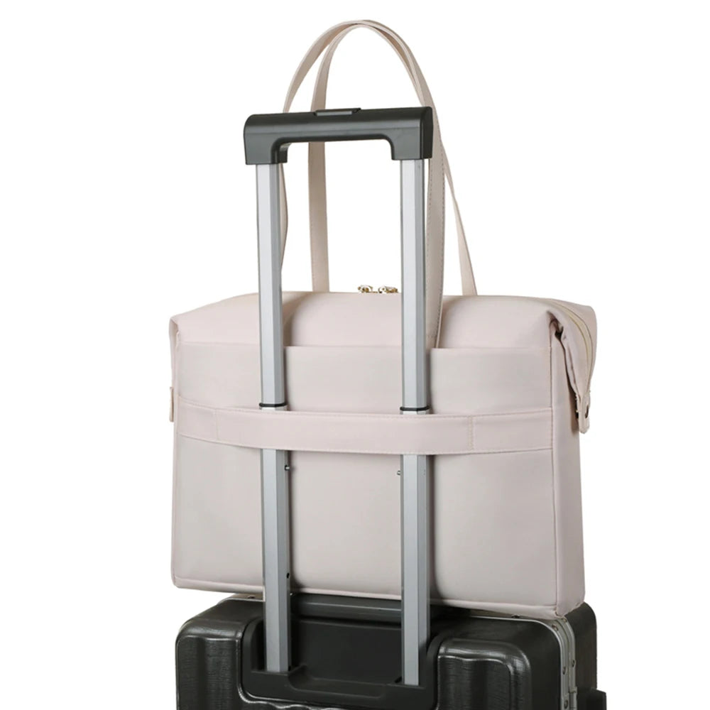 A light beige tote bag with a telescoping silver handle, shown resting on top of a black rolling suitcase against a plain white background.