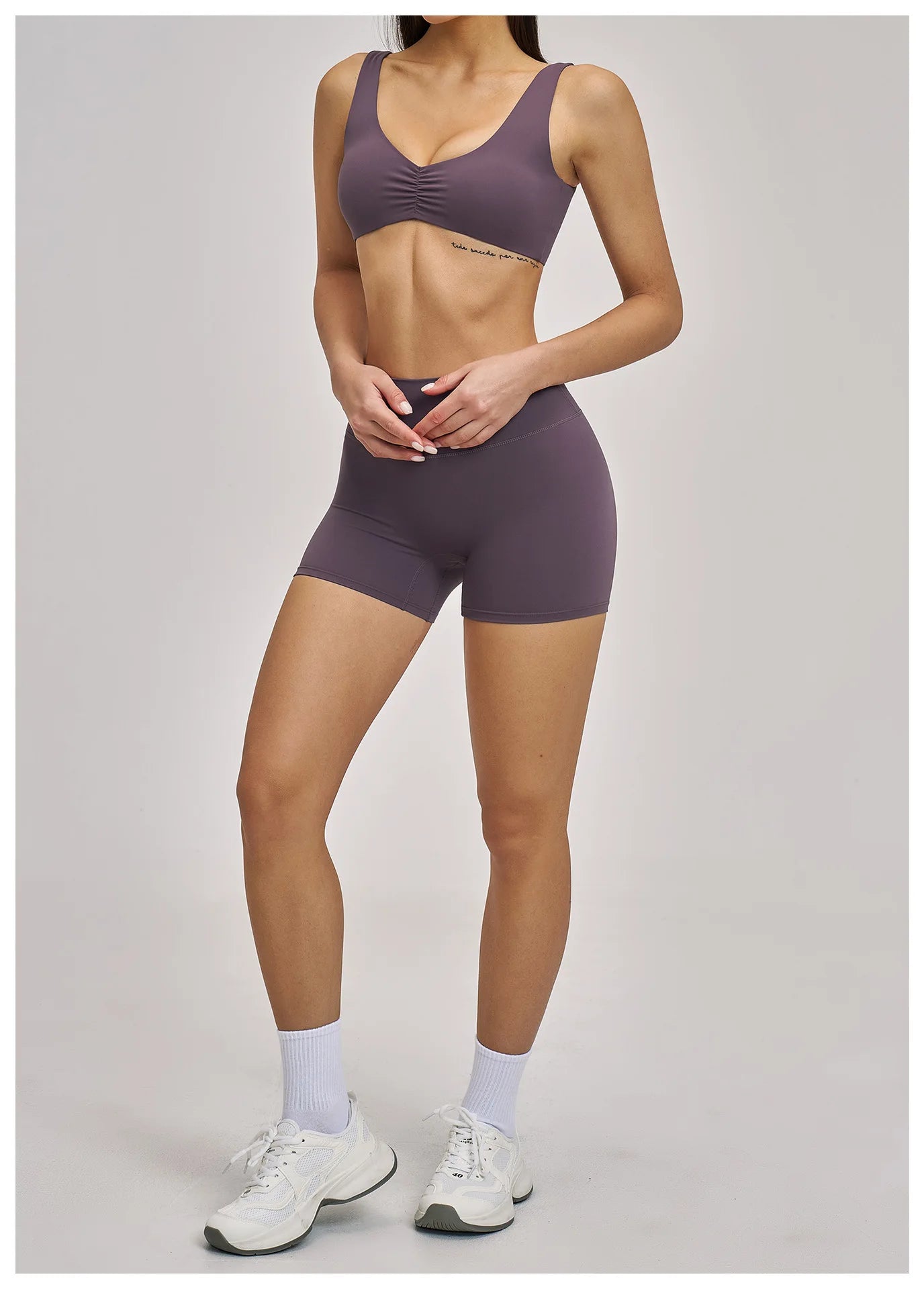 Person wearing a matching purple sports bra and shorts set on a plain background