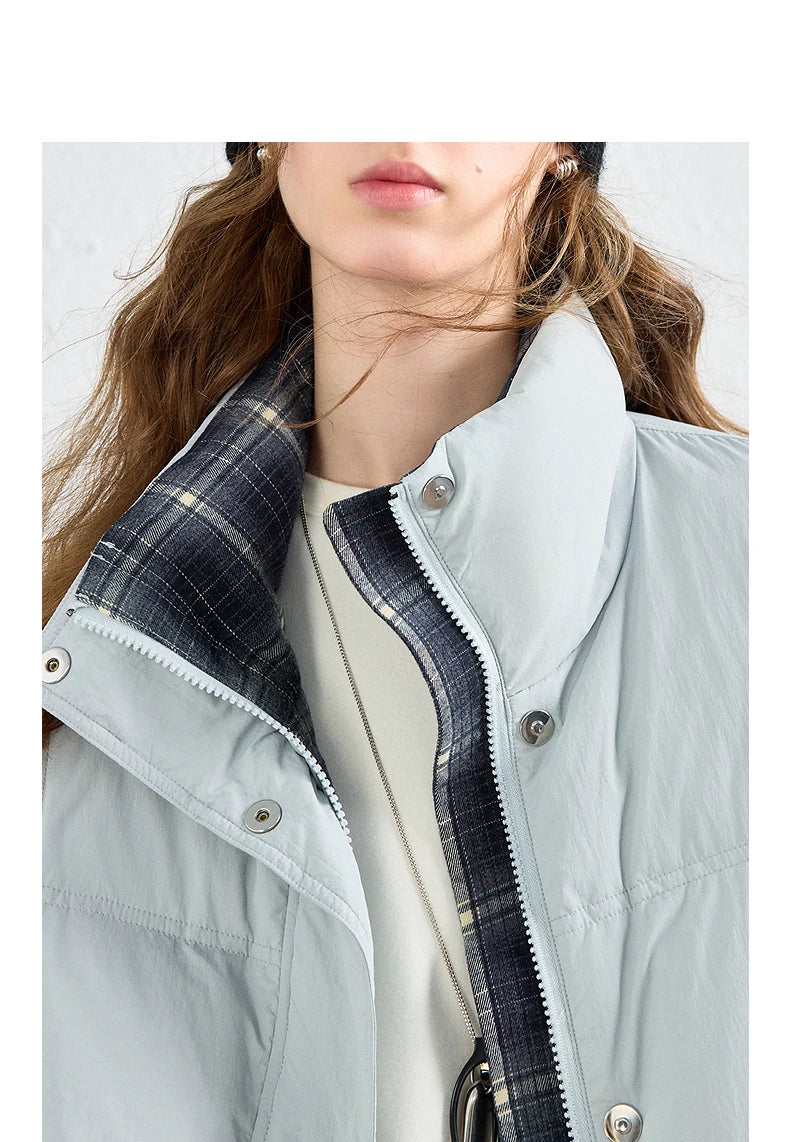 Close-up of a model wearing a light gray puffer vest with a dark navy plaid lining on the collar and zipper trim, layered over a cream top.