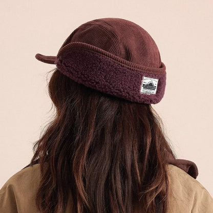 Brown knitted headband with a logo worn by a person on a beige background